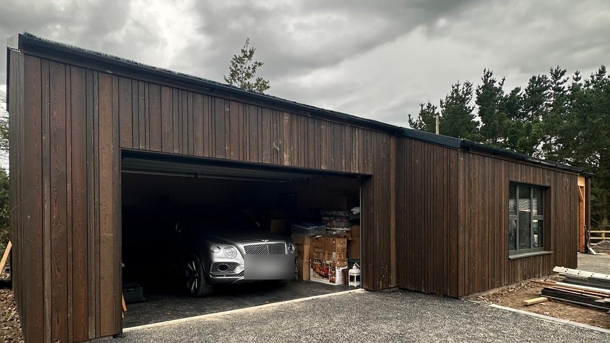 A finished timber frame quad garage and gym, clad in vertical timber, adding space to a family home