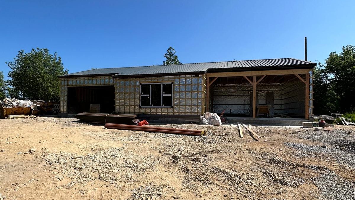 A timber frame extension shell with the roof on and the walls wrapped, ready for windows and cladding